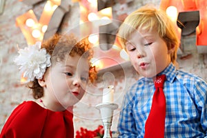 Little happy girl and boy blow out white candle, photo