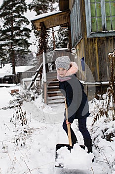 Little happy girl cleans snow near a his rural house