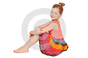 Little happy girl in colorful skirt sits, isolated on white background