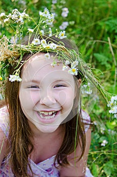 Little happy girl in a garland of field flowers