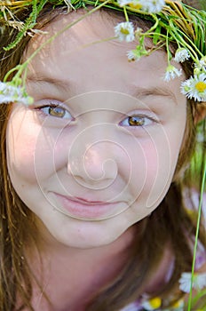 Little happy girl in a garland of field flowers