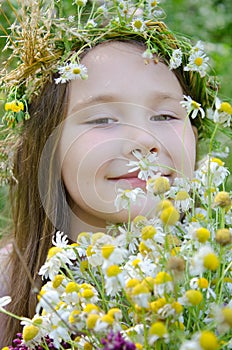 Little happy girl in a garland of field flowers