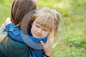 Little happy girl hugs her mom and tells her something in the ear in the park