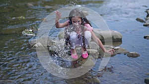 Little happy girl is playing near the river. Squirting water at the camera.