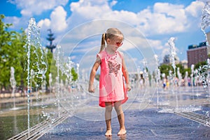 Little happy girl playing in open street fountain