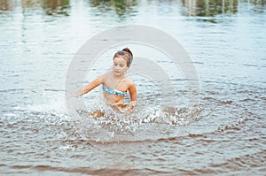 Little happy girl plays with water and splashes of water in the sea