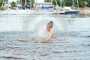 Little happy girl plays with water and splashes of water in the sea