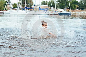 Little happy girl plays with water and splashes of water in the sea