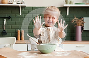 Little happy girl prepares dough in the kitchen. Hands in flour. Child pastry chef in the kitchen