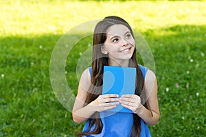 Little happy girl reading book outdoors sunny day, daydreamer concept