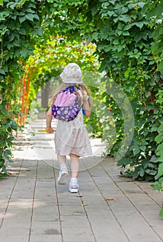 Little happy girl runs cheerfully along the green sunny alley