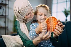 Little happy girl sitting on the sofa at home, playing poppit game together with her mother