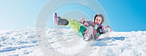 Little Happy girl slides down from the snow slope with blue sky