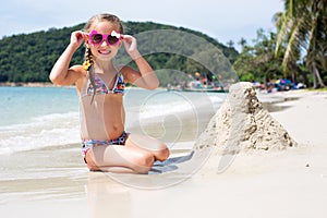 Little happy girl in sunglasses and a swimsuit in the sea. Concept of relaxation and vacation.Girl playing sand on the seashore