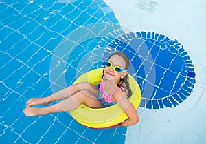 Little happy girl swimming in the outdoor pool on an inflatable yellow circle with diving glasses on a Sunny summer day