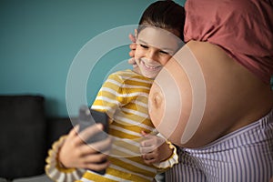 Little happy girl takes a picture of herself and her mother`s belly