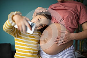 Little happy girl takes a picture of herself and her mother`s belly