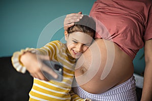 Little happy girl takes a picture of herself and her mother`s belly