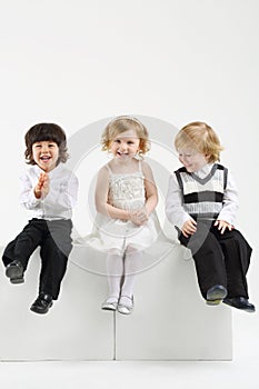 Little happy girl and two boys sit on white big