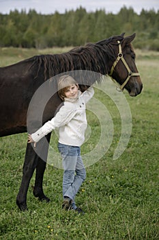 Little happy girl in a white sweater standing and hugging the horse warm autumn day. Lifestyle portrait