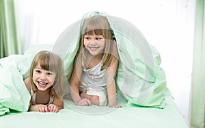 Little happy girls lying under blanket on bed