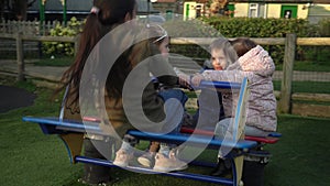 Little Happy group Children Different Ege have fun spinning on merry-go-round. Smiling Siblings friends playing outside