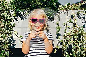 Little happy laughing blonde girl in sunglasses looks at the camera.