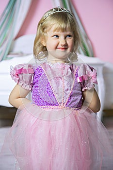 Little happy princess girl in pink dress and crown in her royal room posing and smiling.