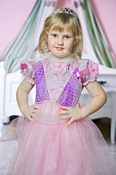 Little happy princess girl in pink dress and crown in her royal room posing and smiling.