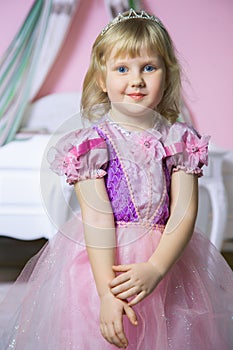 Little happy princess girl in pink dress and crown in her royal room posing and smiling.