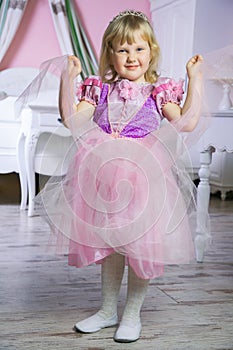 Little happy princess girl in pink dress and crown in her royal room posing and smiling.