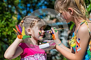 Little happy sisters play with colors in the park, children play, children paint each other