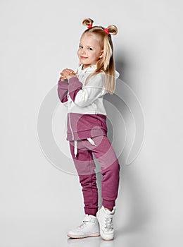 Little happy smiling girl posing in sportswear and sneakers on gray background.