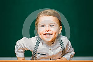 Little happy student boy. Cute preschooler is sitting at a desk indoors. Individual tutoring. Friendly child in