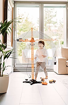 Little happy toddler boy playing with big construction building crane toy at home in living room.