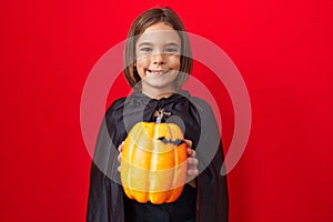 Little hispanic boy wearing a cape and holding halloween pumpkin thinking attitude and sober expression looking self confident