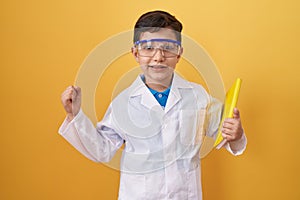 Little hispanic boy wearing scientist glasses screaming proud, celebrating victory and success very excited with raised arm