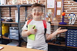 Little hispanic boy wearing student backpack and holding book at school class celebrating achievement with happy smile and winner