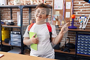 Little hispanic boy wearing student backpack and holding book at school class smiling happy pointing with hand and finger to the