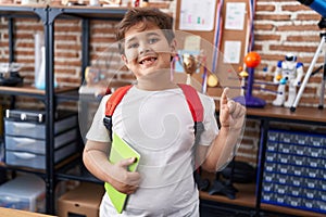 Little hispanic boy wearing student backpack and holding book at school class smiling with an idea or question pointing finger