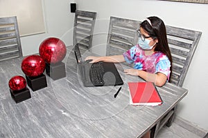 Little Hispanic girl doing school at home with glasses and face masks due to the quarantine of the Covid-19 pandemic due to corona