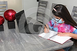 Little Hispanic girl doing school at home with glasses and face masks due to the quarantine of the Covid-19 pandemic due to corona