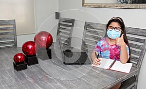 Little Hispanic girl doing school at home with glasses and face masks due to the quarantine of the Covid-19 pandemic due to corona
