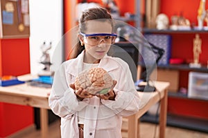 Little hispanic girl holding brain at science class at school clueless and confused expression