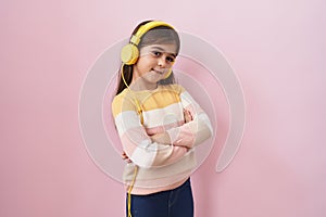 Little hispanic girl listening to music using headphones happy face smiling with crossed arms looking at the camera