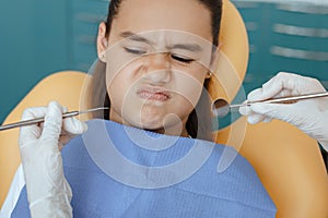 Little hispanic girl in medical chair looks with disbelief at instruments in hands of doctor