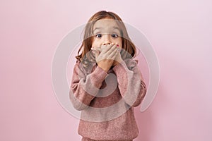 Little hispanic girl standing over pink background shocked covering mouth with hands for mistake