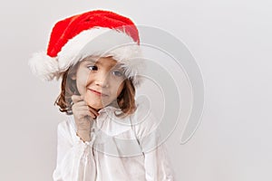 Little hispanic girl wearing christmas hat thinking concentrated about doubt with finger on chin and looking up wondering