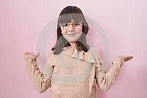 Little hispanic girl wearing glasses clueless and confused expression with arms and hands raised