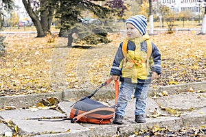 Little hooligan boy dragged away his mother`s backpack and make grimace at her in autumn city Park